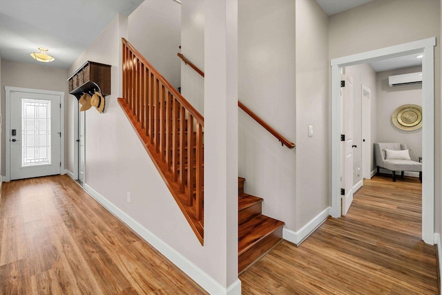 foyer with stairway, a wall mounted air conditioner, baseboards, and wood finished floors