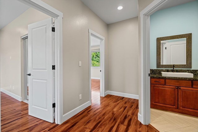 hall with light wood-style floors, baseboards, and a sink