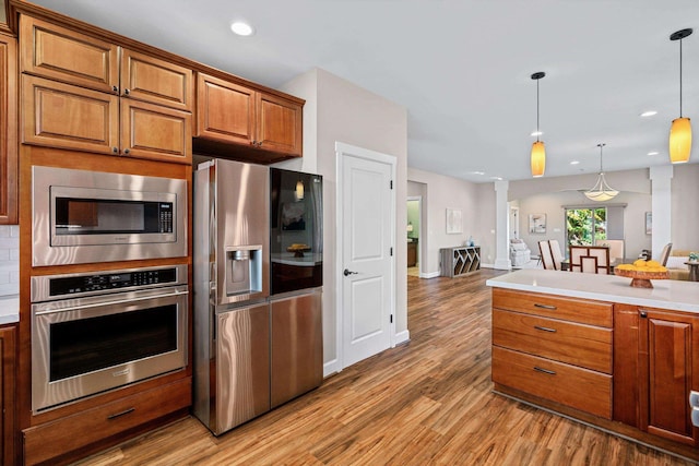 kitchen with brown cabinetry, ornate columns, light wood-style flooring, hanging light fixtures, and appliances with stainless steel finishes