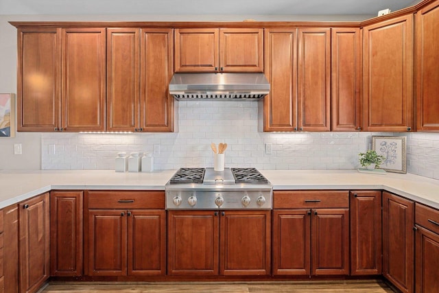 kitchen featuring light countertops, tasteful backsplash, under cabinet range hood, and stainless steel gas cooktop