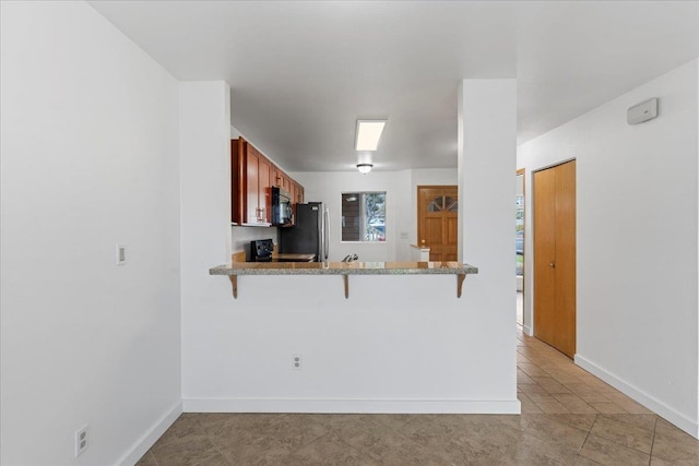 kitchen featuring black electric range, stainless steel fridge, a kitchen breakfast bar, kitchen peninsula, and light stone countertops