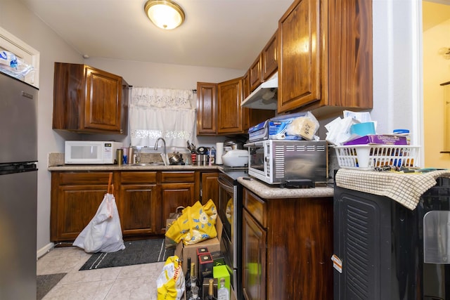 kitchen with brown cabinetry, under cabinet range hood, a sink, appliances with stainless steel finishes, and light tile patterned floors
