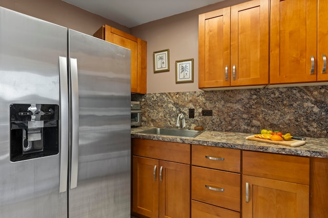 kitchen with sink, stainless steel refrigerator with ice dispenser, dark stone counters, and tasteful backsplash