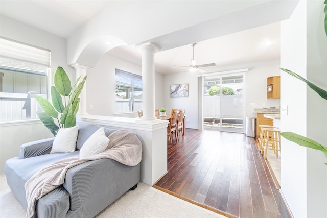 living room featuring decorative columns, plenty of natural light, a ceiling fan, and dark wood-style flooring