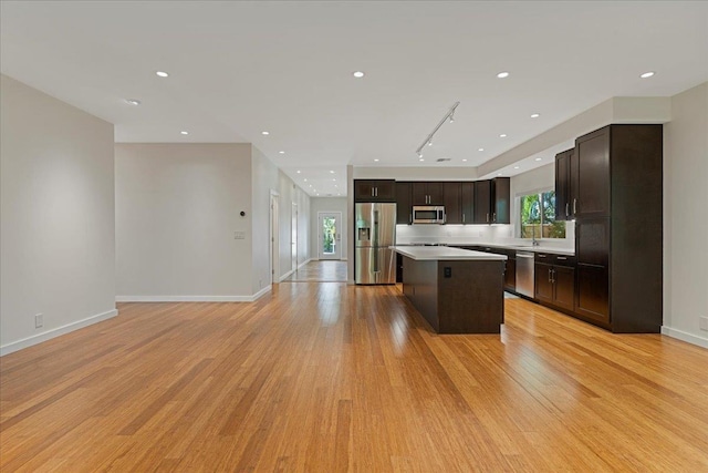 kitchen with light countertops, a kitchen island, appliances with stainless steel finishes, light wood-style flooring, and dark brown cabinets