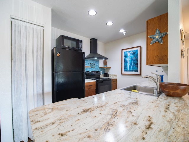 kitchen featuring light stone countertops, black appliances, wall chimney range hood, sink, and tasteful backsplash