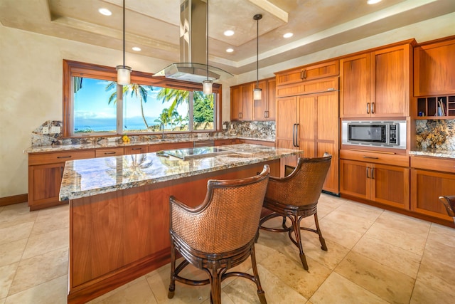 kitchen with built in appliances, decorative light fixtures, a tray ceiling, and light stone countertops