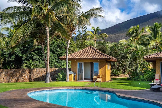 view of swimming pool with a lawn, a mountain view, and an outbuilding