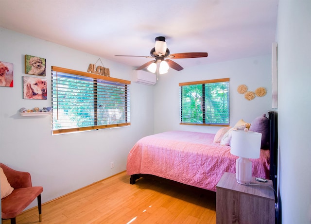 bedroom with ceiling fan, a wall unit AC, and wood finished floors