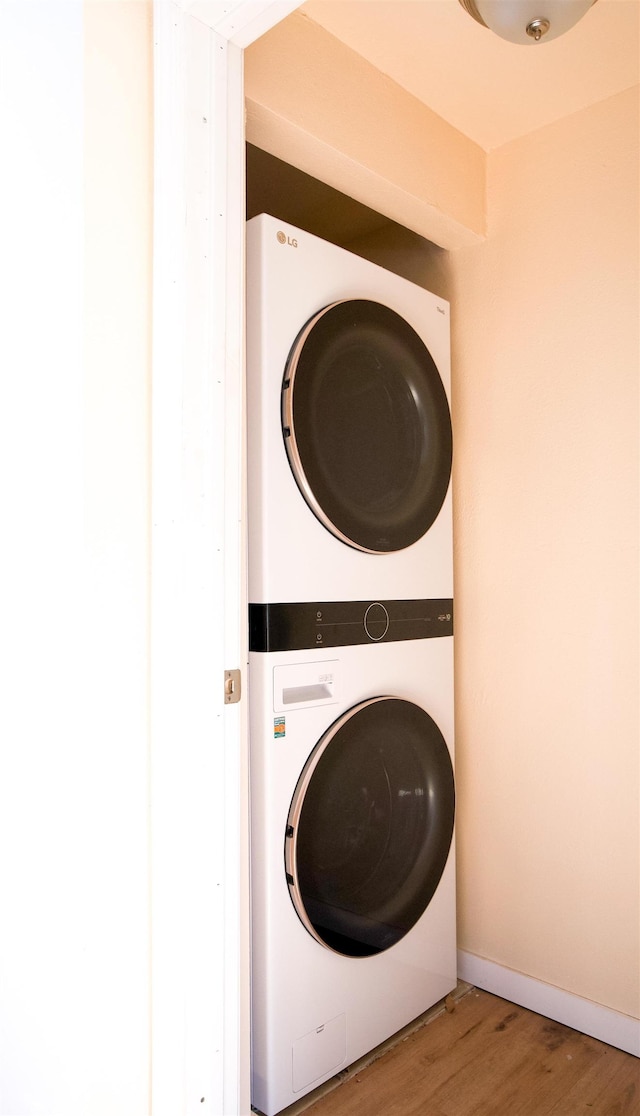 laundry room with laundry area, baseboards, wood finished floors, and stacked washer and clothes dryer