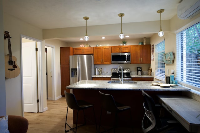 kitchen with a breakfast bar area, stainless steel appliances, hanging light fixtures, a wall mounted AC, and a sink