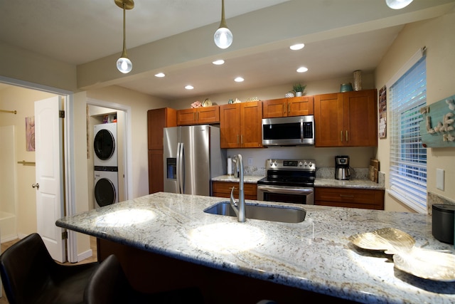 kitchen with decorative light fixtures, a breakfast bar area, appliances with stainless steel finishes, stacked washer / dryer, and a sink