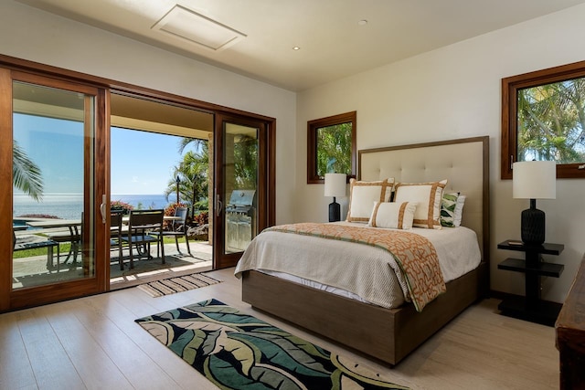 bedroom featuring access to outside, light hardwood / wood-style flooring, and a water view