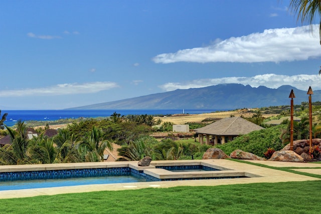 view of swimming pool with a lawn, a mountain view, and an in ground hot tub