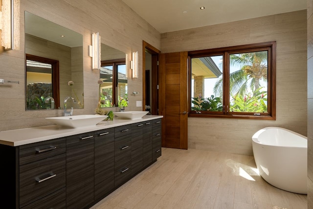 bathroom with wood-type flooring, vanity, tile walls, and a healthy amount of sunlight