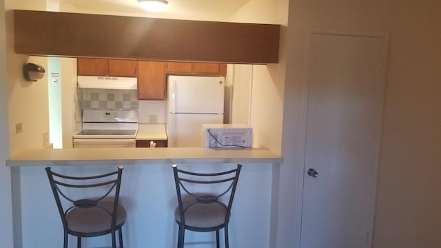 kitchen featuring a breakfast bar, stove, white fridge, and tasteful backsplash