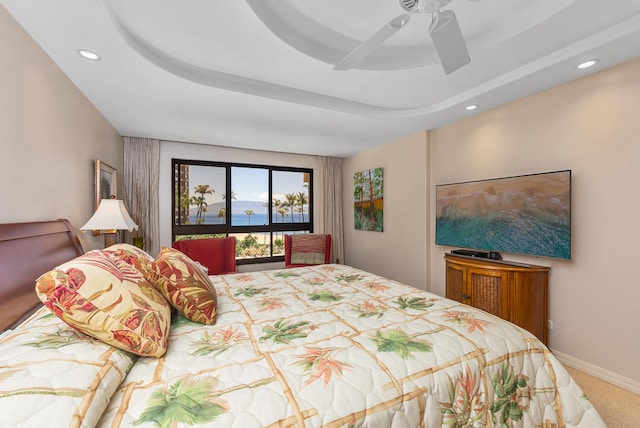 carpeted bedroom with ceiling fan and a tray ceiling