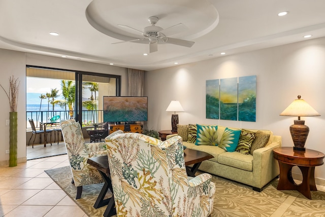 living room featuring light tile flooring, ceiling fan, a water view, and a tray ceiling