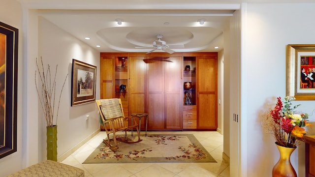 sitting room featuring ceiling fan, light tile floors, and a tray ceiling