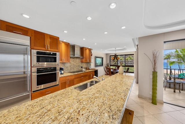 kitchen featuring backsplash, appliances with stainless steel finishes, wall chimney range hood, light tile floors, and sink