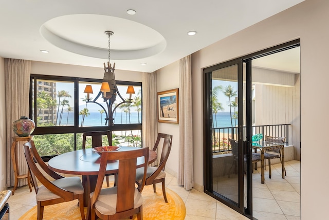 dining space with a notable chandelier, a water view, a raised ceiling, and light tile flooring