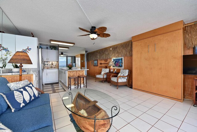 4327 Lower Honoapiilani Rd Unit 207B, Lahaina, HI 96761 - living room featuring ceiling fan, wood walls, light tile patterned floors, and a textured ceiling