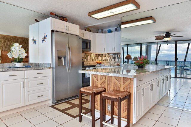4327 Lower Honoapiilani Rd Unit 207B, Lahaina, HI 96761 - kitchen with a breakfast bar, light tile patterned floors, a kitchen island, white cabinetry, and stainless steel appliances
