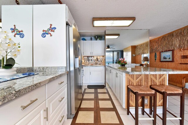 4327 Lower Honoapiilani Rd Unit 207B, Lahaina, HI 96761 - kitchen featuring a breakfast bar, white cabinets, ceiling fan, light stone countertops, and light tile patterned floors