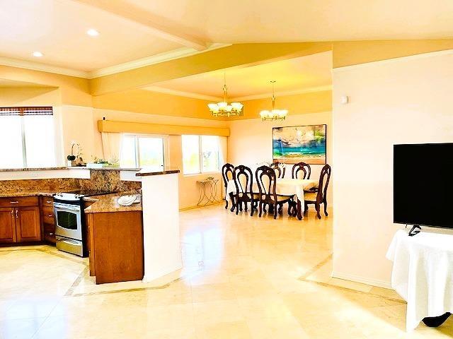 kitchen featuring an inviting chandelier, stainless steel range with electric stovetop, hanging light fixtures, ornamental molding, and dark stone counters