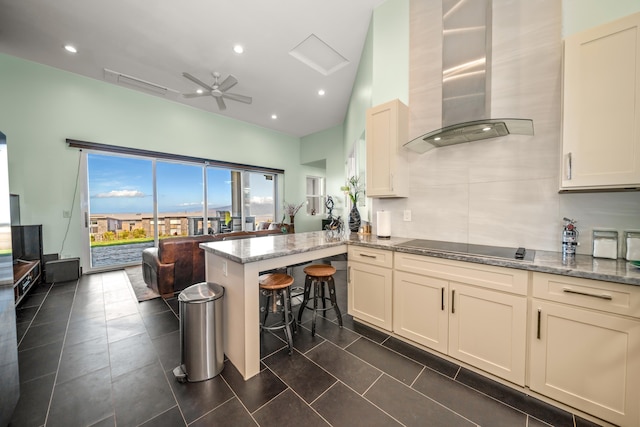 kitchen featuring ceiling fan, wall chimney range hood, light stone counters, kitchen peninsula, and black electric cooktop