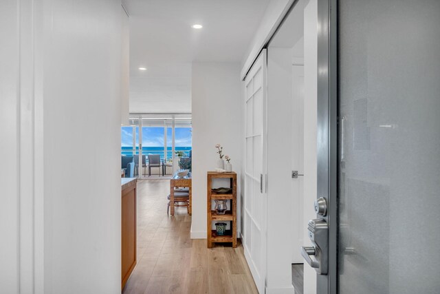 hallway with a wall of windows, light wood-type flooring, and recessed lighting