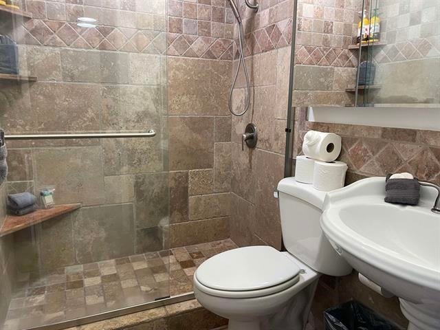 bathroom featuring sink, tiled shower, tile walls, and toilet