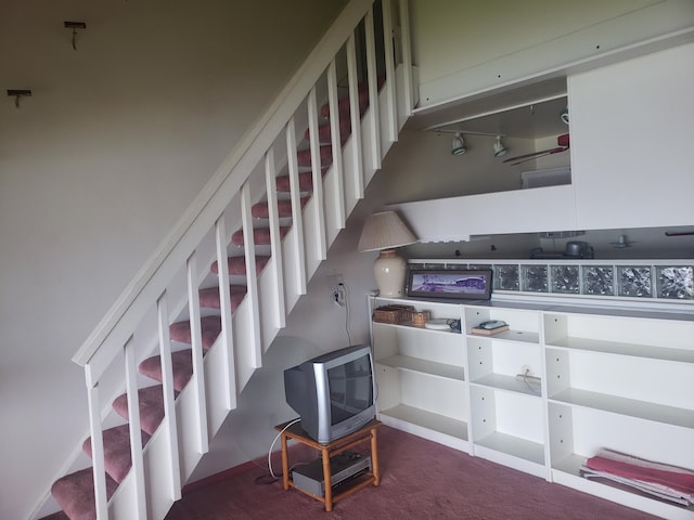 stairs with track lighting and dark colored carpet