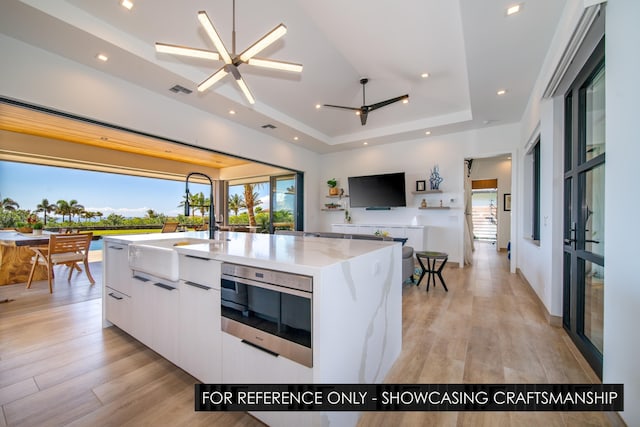 kitchen featuring a tray ceiling, ceiling fan, a sink, modern cabinets, and white cabinetry
