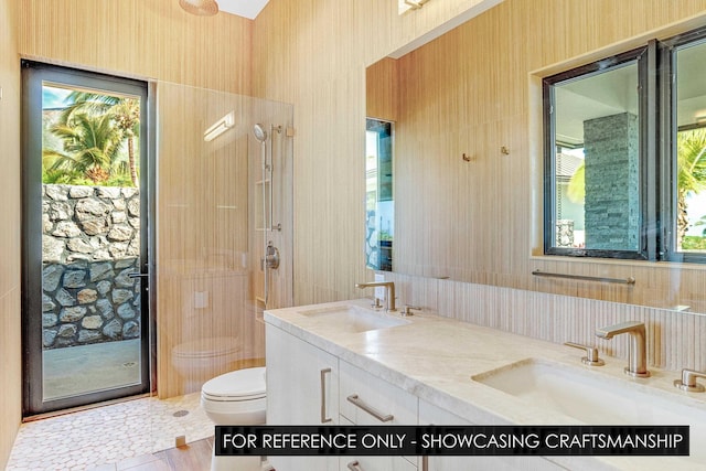 full bath with toilet, plenty of natural light, double vanity, wallpapered walls, and a shower