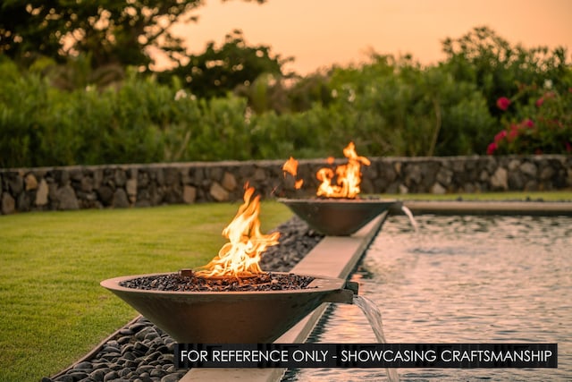 patio terrace at dusk featuring an outdoor fire pit and a lawn