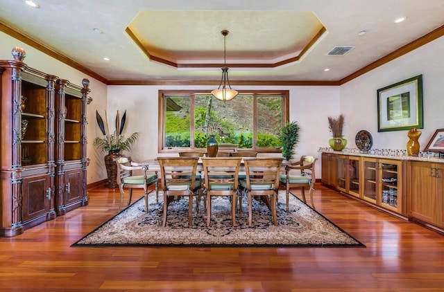 dining area featuring hardwood / wood-style flooring, ornamental molding, and a raised ceiling