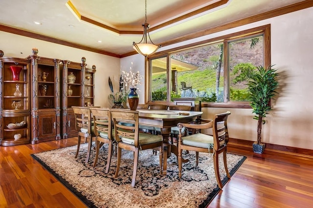 dining space featuring crown molding, wood-type flooring, and a raised ceiling