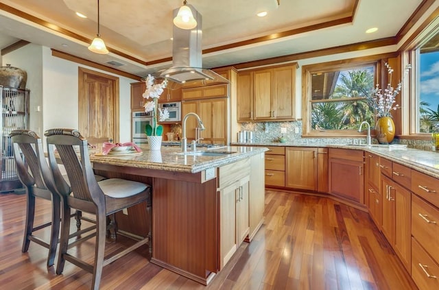 kitchen with oven, pendant lighting, a tray ceiling, and a kitchen island with sink