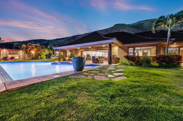 pool at dusk with a mountain view, a lawn, and a patio