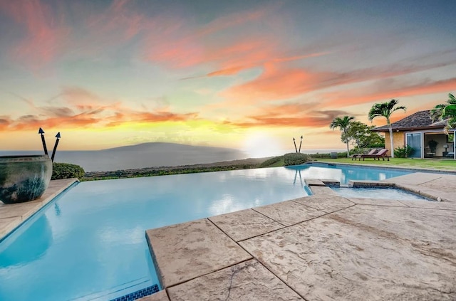 pool at dusk featuring a water view and a patio