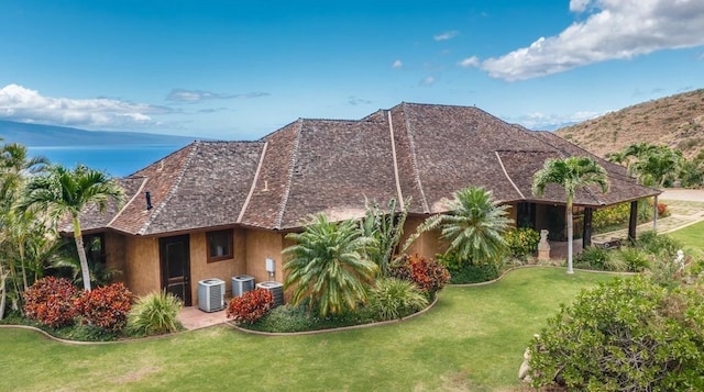 rear view of property with a mountain view, central AC unit, and a yard