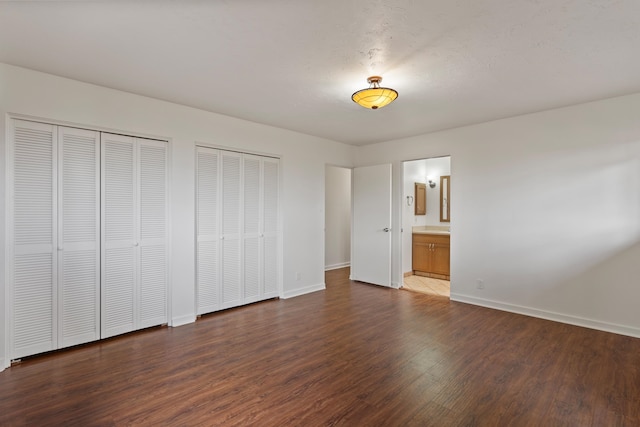 unfurnished bedroom featuring dark hardwood / wood-style flooring, two closets, and connected bathroom