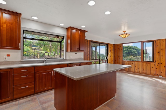 kitchen with wooden walls, light stone countertops, light tile patterned floors, a center island, and sink