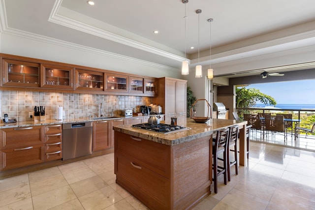 kitchen with pendant lighting, appliances with stainless steel finishes, a kitchen island with sink, light stone countertops, and a raised ceiling