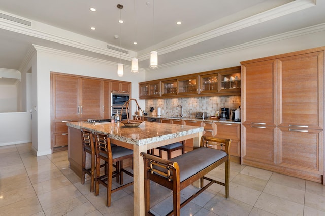 kitchen featuring sink, hanging light fixtures, black microwave, light stone countertops, and a center island with sink