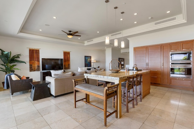 kitchen featuring decorative light fixtures, built in microwave, an island with sink, oven, and a tray ceiling