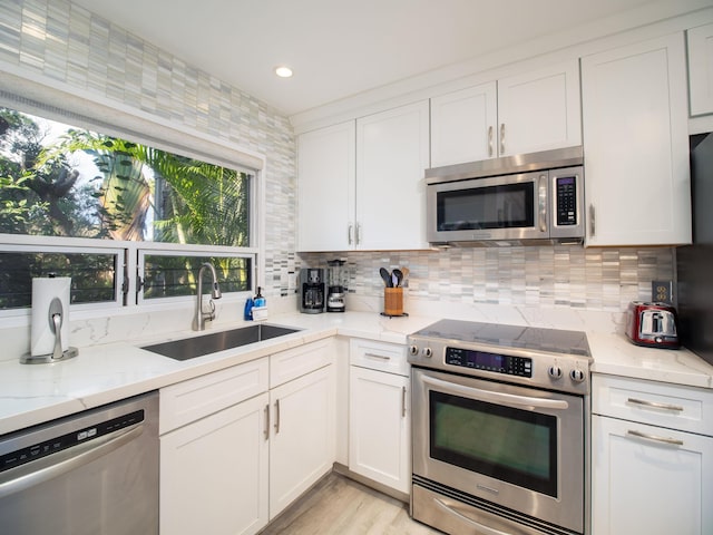 kitchen featuring sink, tasteful backsplash, light stone counters, white cabinetry, and stainless steel appliances