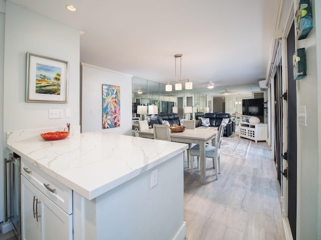 kitchen with light stone countertops, hanging light fixtures, kitchen peninsula, crown molding, and white cabinets