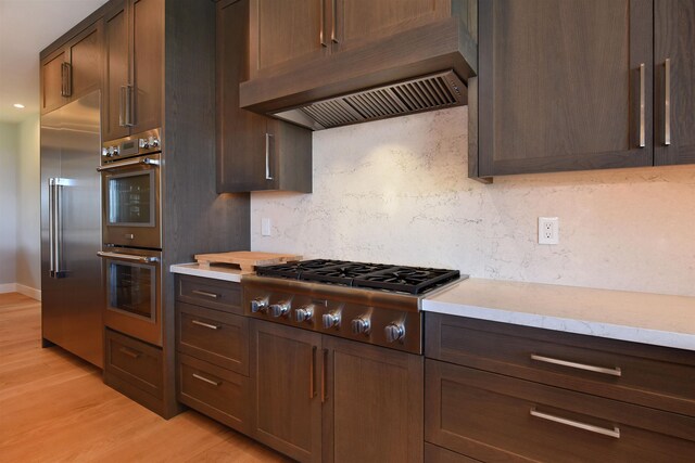 kitchen with light stone counters, appliances with stainless steel finishes, dark brown cabinetry, and light wood-type flooring